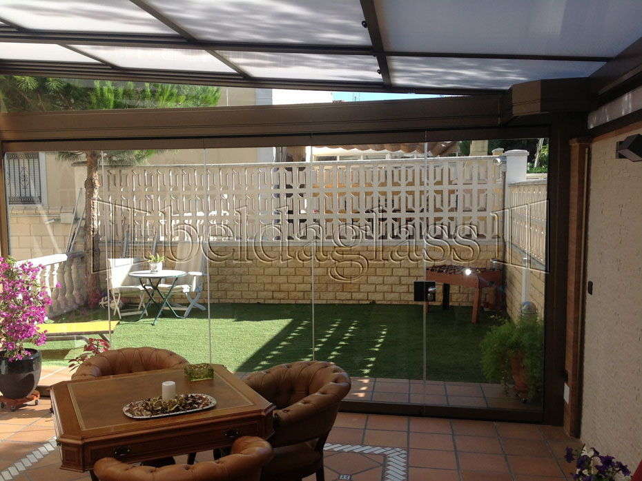 Beldaglass realiza una instalación de cerramiento de terraza con techo móvil de policarbonato y cortinas de cristal sin guía al suelo en Madrid.¡ Llámanos!