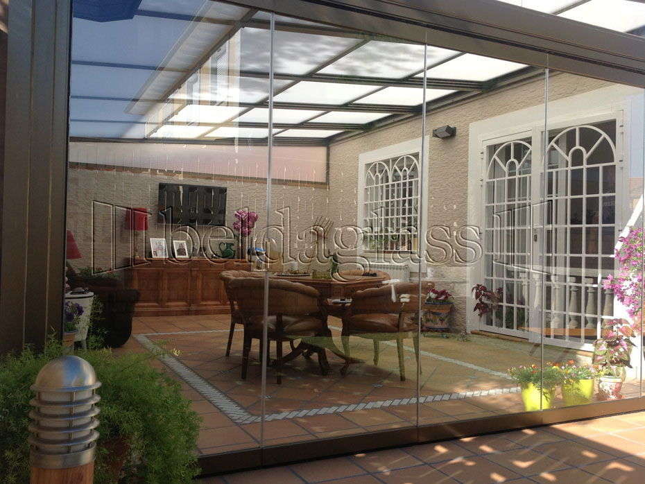 Beldaglass realiza una instalación de cerramiento de terraza con techo móvil de policarbonato y cortinas de cristal sin guía al suelo en Madrid.¡ Llámanos!